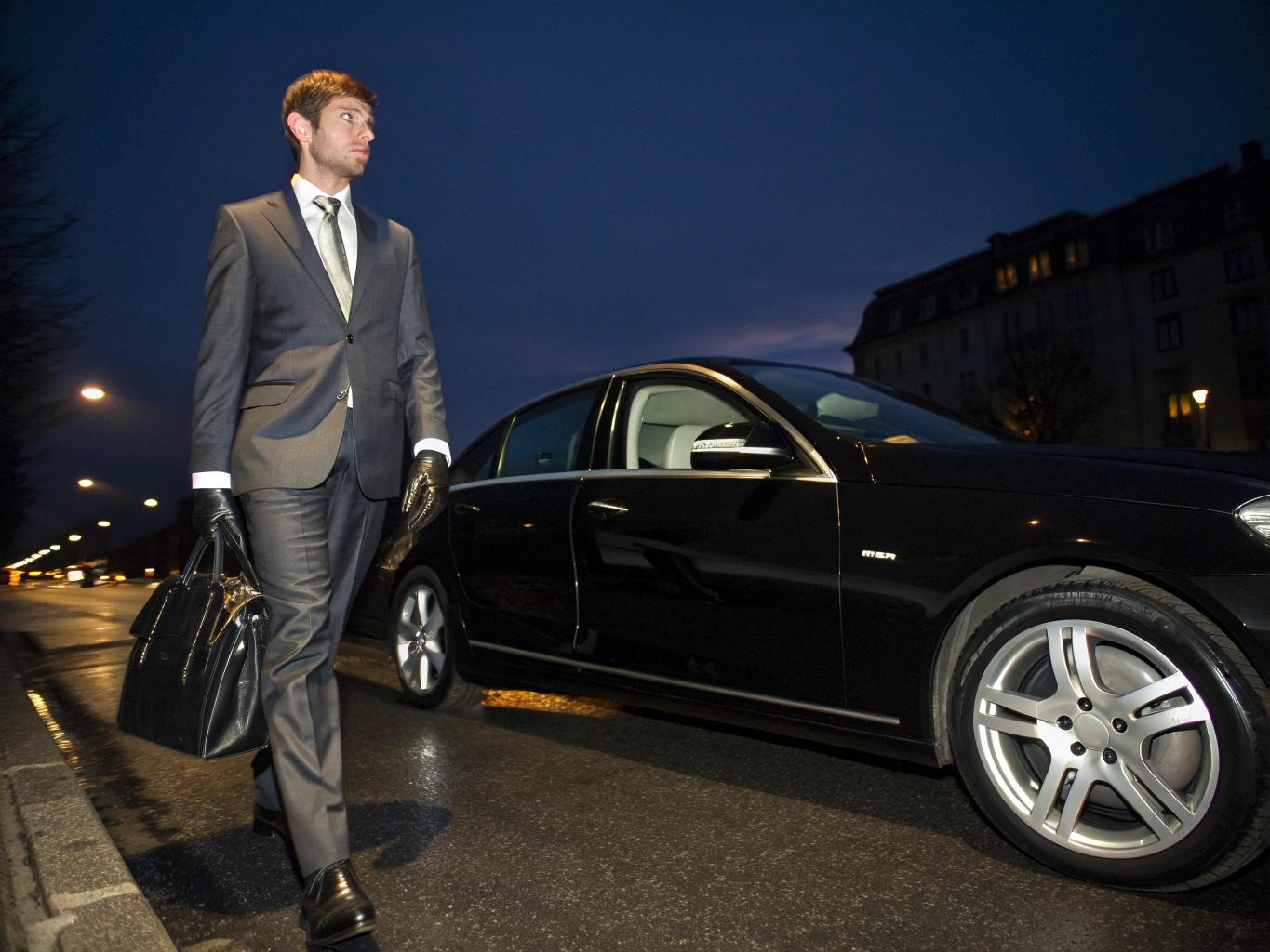 Professional private chauffeur standing by luxury Mercedes sedan.